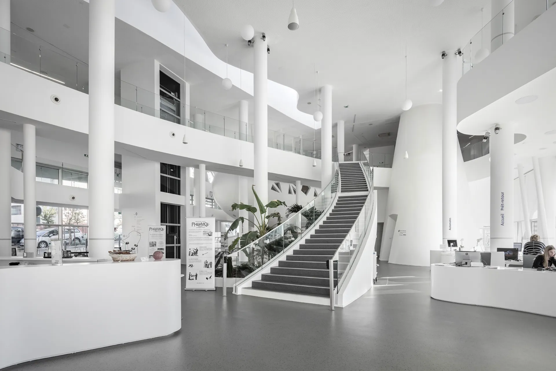 Accueil de médiathèque avec escalier central et mobilier sur mesure